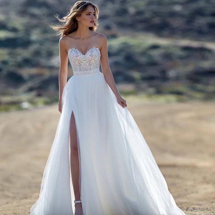 Modella con abito da sposa senza spalline, corpetto di pizzo, gonna in tulle spaccata e colline sullo sfondo