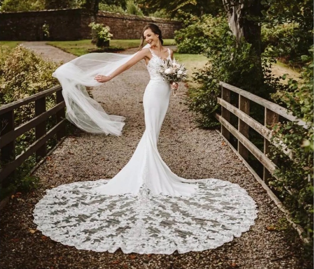 Sposa in abito a sirena L'Abito Perfetto con strascico di pizzo e velo al vento su un ponticello in legno